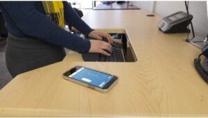 Woman working on tilting keyboard tray with smartphone to the right