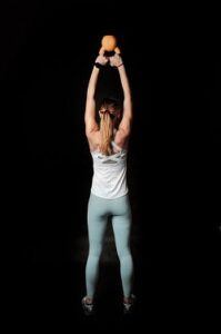 Back view of a woman lifting a hand weight above her head with arms straight