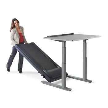 Woman rolling a lifeSpan treadmill underneath an adjustable standing desk