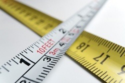 A white tape measure makes a cross shape against a yellow tape measure
