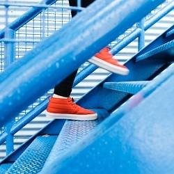 Red sneakered feet climbing blue metal stairs