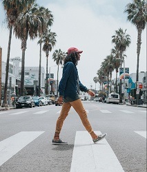 Man walks across a zebra crossing with palm trees and buildings in the background