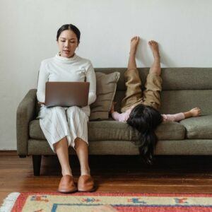 Woman working on laptop whilst sitting on sofa next to a child