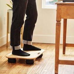 Bottom half of person standing on a balance board next to a desk