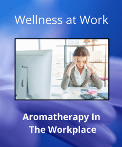 Woman holding head in hands at desk within text reading "workplace wellness, aromatherapy in the workplace"