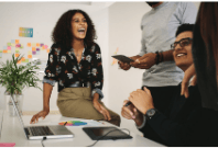 Woman sitting on a desk laughing and appearing to have fun with colleagues