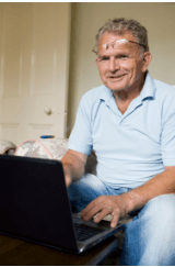 Gentleman of advanced years smiles as he types onto a laptop