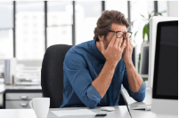 Man sat at desk looking stressed with his face in his hands