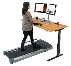 Woman works at a height adjustable desk whilst walking on the iMovR ThermoTread GT treadmill