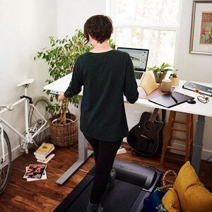 Back view of woman working at desk whilst walking on a treadmill
