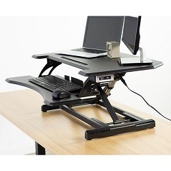 Black standing desk converter on a light wood desktop