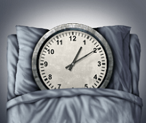 Clock resting on pillows slightly covered by a bedsheet